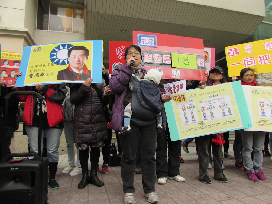 幼保幼教學界聯盟今(19)日來到立法院前抗議日前朝野協商《幼照法》結果。圖為一名家長背著孩子呼籲，有執照的老師才能帶大班。圖：邱珮文/攝