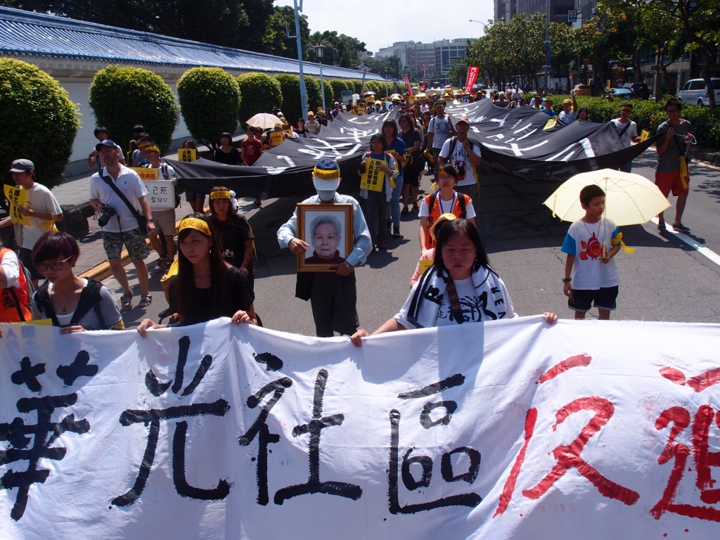 約2、30位華光社區居民以及聲援團體、民眾數百人，頭綁「華光反迫遷」黃布條，手拉「國土活化成商品，人民被告淪債奴」巨大黑色布條，在正中午烈日下緩緩往凱道前進。圖：陳柔伊/攝