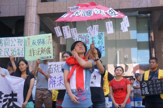 公視前派遣工陳盈潔被榜上大紅蝴蝶結，勞動部試圖要幫他撐傘，但傘面卻充滿了破洞，暗喻根本沒有所謂的轉正納編，「只是欺騙勞工的幌子、是一把根本保護不了勞工的破傘」。 圖：張容瑄/攝