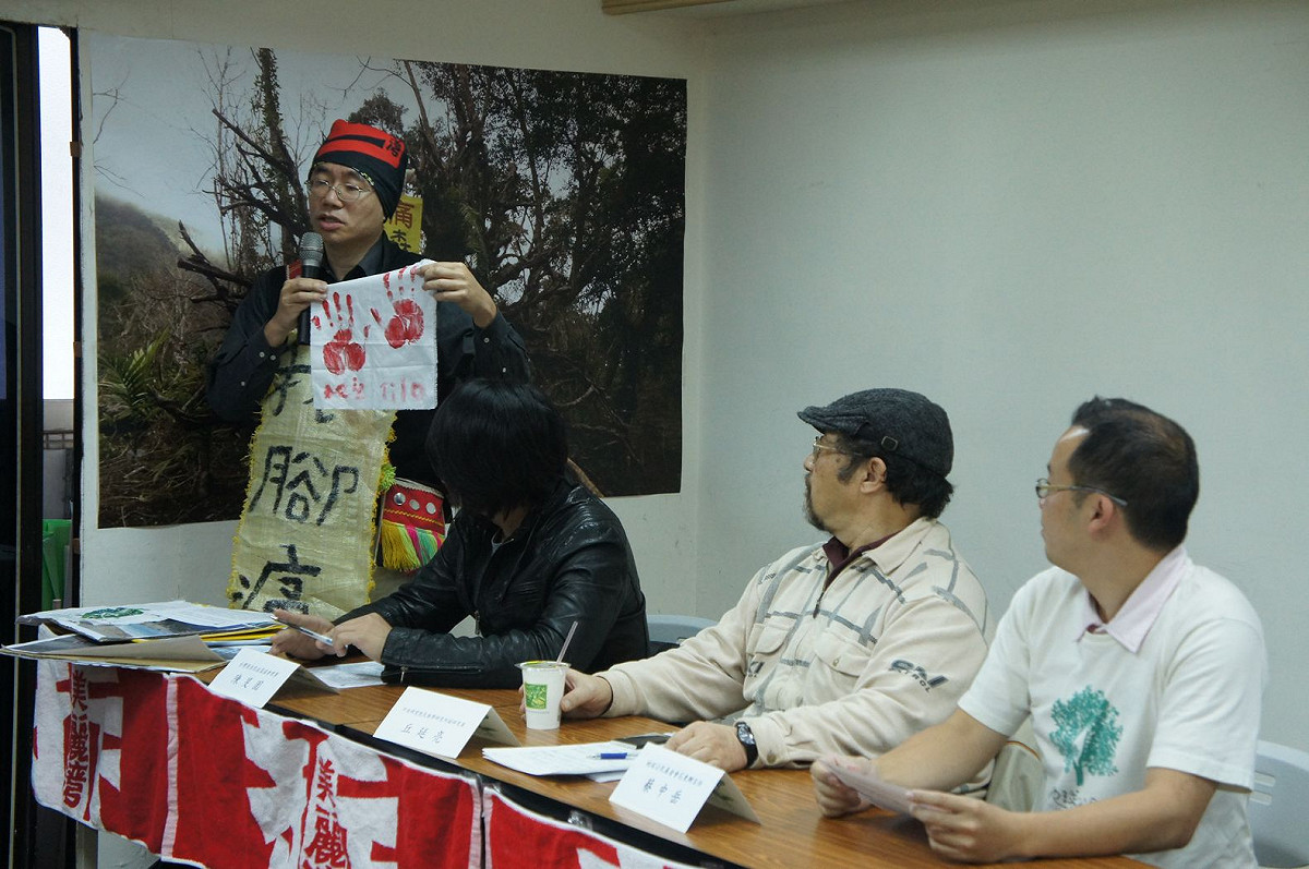 台灣原住民族部落行動聯盟成員拔尚今日在記者會中，展示身上披掛的用廢棄麻布袋製作的「我腳痛」簡易布條，手持部落青年的手掌拓印；拔尚解釋，隊員的「痛」其實也是「疼惜」、對土地的愛。圖：汪彥成/攝