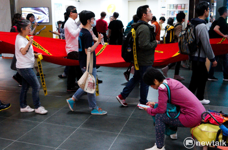 遊行隊伍拉著象徵中國極權的紅布條走進台北火車站，同時高喊：『言論自由李明哲無罪』口號，但一位坐在一旁的旅客似乎不為所動，低頭看著她的手機。   圖：張良一 /攝
