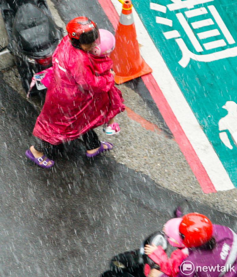 台北市區傍晚雷聲大作，緊接著嚇了一場雷陣雨，一位騎機車載小孩的媽媽，來不及幫女兒穿雨衣，趕緊抱她到旁邊的雨棚避雨。   圖：張良一/攝