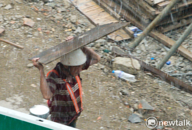 一位建築工人面對突如其來的大雨，趕緊用木板擋雨。   圖：張良一/攝