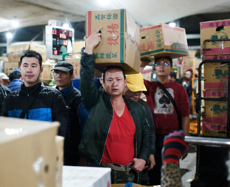 本報特約攝影記者張良一獲2019台灣新聞攝影大賽「年度最佳新聞攝影作品集」等四個獎項，圖為年度最佳新聞攝影作品集作品之一的拖工在北農第一果菜批發市場搬運已標得的蔬菜。   圖：張良一/攝