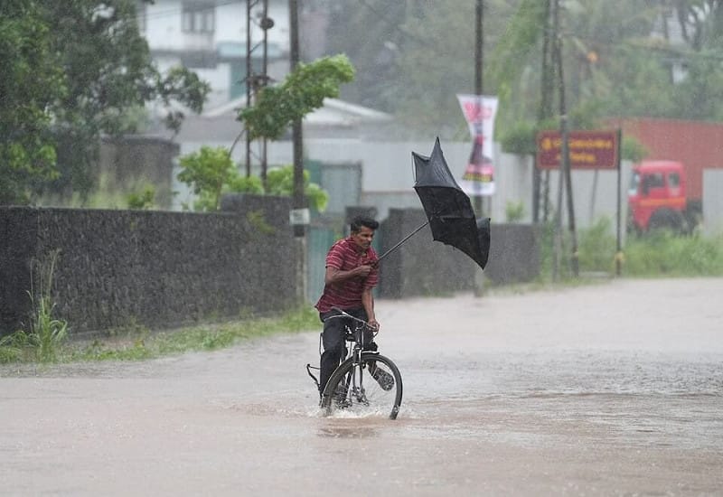 氣旋迪特瓦在斯里蘭卡帶來豪雨及洪患，一名男子28日騎自行車行經積水的街道時，雨傘被強風吹壞。（路透社）   