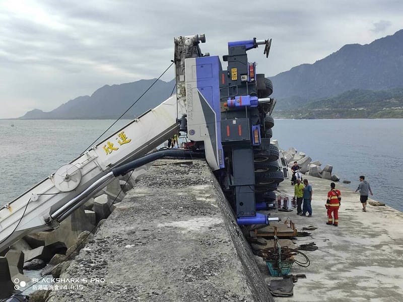 台東成功漁港30日中午一輛吊車在碼頭吊掛消波塊時不慎翻覆，吊臂卡進海中消波塊間，車體翻覆堤防，車內2人受困，警消獲報到場1人OHCA，1人經器材破壞後獲救送醫。（民眾提供）中央社記者李先鳳傳真　114年11月30日   