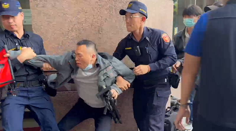 游智彬拿「生死狀」鬧場被警方架走。 圖:高逸帆/翻攝 游智彬拿「生死狀」鬧場被警方架走。 圖:高逸帆/翻攝