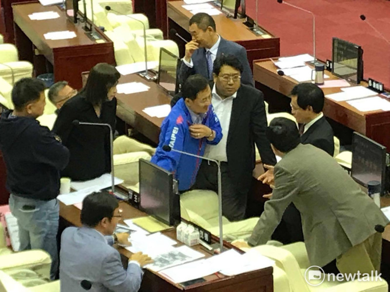 議長宣布休息時間，台北市副市長陳景峻（身穿藍色外套）、鄧家基（咖啡色西裝背對者）趕緊上前與民進黨議員協調。   圖：周煊惠 / 攝