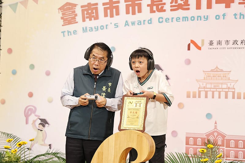 台南市政府今日舉辦市長獎頒獎典禮，由於黃偉哲任期也將在年底屆滿，今年典禮以「市長畢業趴」為主題，現場設置拍照背板及驚喜紀念禮物，也有不少學生帶來親手製作要送市長的畢業禮物，包括寫有「偉哲市長畢業快樂」的小布條以及書法作品等，讓黃偉哲相當感動。&nbsp;&nbsp;&nbsp;圖：台南市政府提供