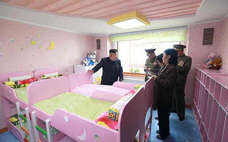 北韓領導人金正日正在視察平壤一處甫完工的孤兒院及幼兒園，背後的玩偶卻意外搶走了金正恩的威風。   圖／翻攝自新華網