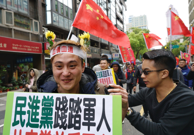 一位統促黨成員頭插兩朵黃菊花，手舉「民進黨踐踏軍人」牌子參與遊行。   圖：張良一/攝