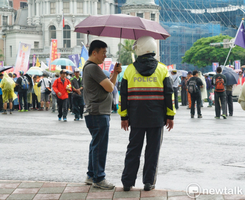 退休警察遊行到行政院前正巧下雨，一位退警幫執勤的員警撐傘。   圖 : 張良一 / 攝