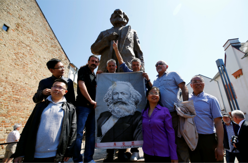德國和中國遊客，拿著馬克思的肖像，在雕像前合影。   圖：達志影像/路透社
