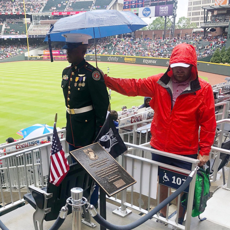 一名穿著紅色夾克、留著鬍子的男子，左手拿著綠色背包，右手則隔著柵欄為站崗少年撐著一把深藍色雨傘。   圖：翻攝自勇士隊推特帳號