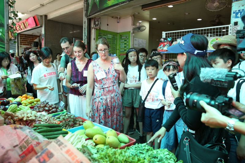 明珠媽媽向凱瑟琳說明東南亞蔬果攤上的食材如何料理。   圖：瑪利亞基金會/提供