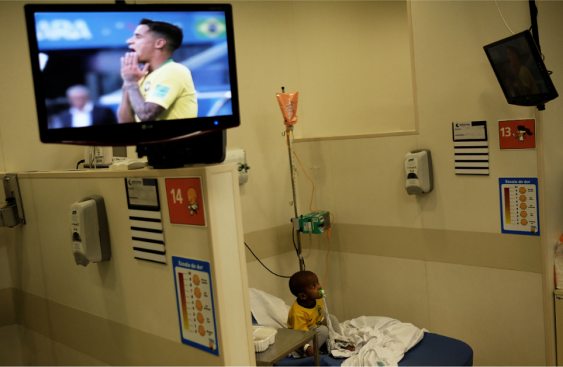2018年俄羅斯世界盃足球賽16強淘汰賽，今天由尋求隊史第6座冠軍的巴西，對戰同樣來自南美的墨西哥，兩隊過去4度在世界盃交手，巴西攻下11球，墨西哥的進球數則尚未開張。圖為遠在巴西聖保羅的癌症兒童醫院，一名3歲的小男孩盧卡斯，穿著巴西球衣T-恤，聚精會神地為自己國家的足球隊加油。「森巴軍團」曾5次奪冠，是世界盃史上最多，足球也成了巴西的「國球」。   圖：達志影像/路透社