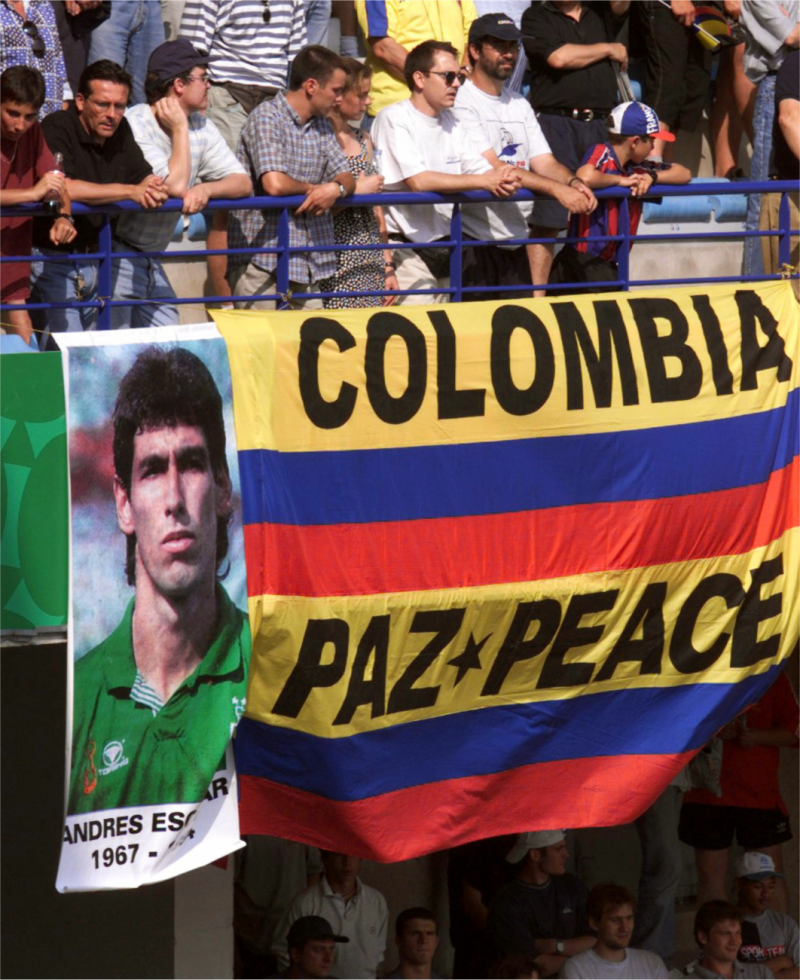 1998年6月22日，法國世界盃小組賽第一輪，哥倫比亞球與突尼西亞之戰。哥國球迷在看台懸掛哥倫比亞前國腳艾斯科巴(Andres Escobar）的肖像，以「和平踢球」為訴求。四年前的同一天的上一屆世界盃，艾斯科巴因一記烏龍球送給地主國美國隊一分，使得球隊吞敗。返國後，7月2日凌晨，他遭人開了12槍送醫不治，年僅27歲。據稱這起命案，是由涉賭而血本無歸的毒梟派人所犯下的。   圖：達志影像/路透社