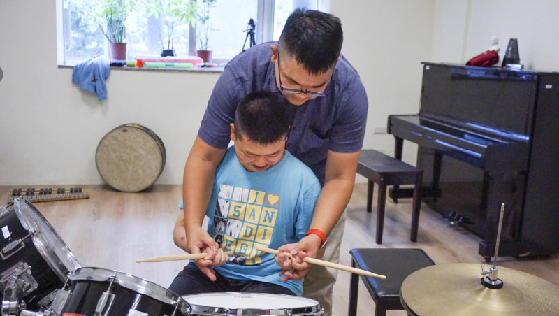 逢甲大學管樂團成員教導瑪利亞青年學習爵士鼓。   圖：網銀基金會/提供