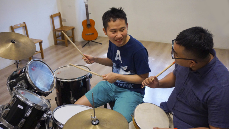 逢甲大學管樂團成員教導瑪利亞青年學習爵士鼓。   圖：網銀基金會/提供