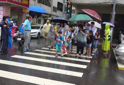 迎接30日開學日，高雄市教育局長范巽綠（撐綠傘者）
打著傘陪同小朋友過馬路，一起歡喜上學去。   圖：中央社