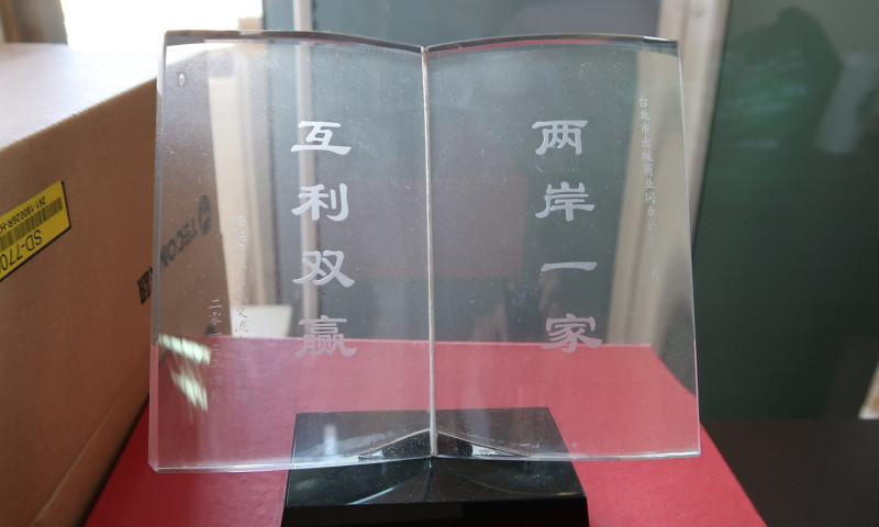 台北市出版商同業公會公會會議室一旁，也擺著一個獎牌，上面寫的「兩岸一家，互利雙贏」，由海協會於2015年贈送給台北市出版商同業公會。   圖：林朝億/攝