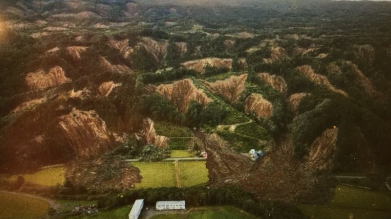 北海道厚真町因地震造成山崩模樣，茶色山麓赤裸裸地露出土砂面，跟原來的綠色混合交錯   圖：劉黎兒翻攝自日本媒體