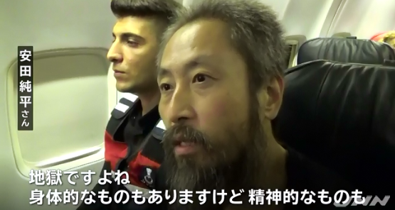 日本記者安田純平（右）遭激進蓋達組織綁架3年多獲釋，在安全人員保護下搭機回日本。   圖：翻攝TBS NEWS