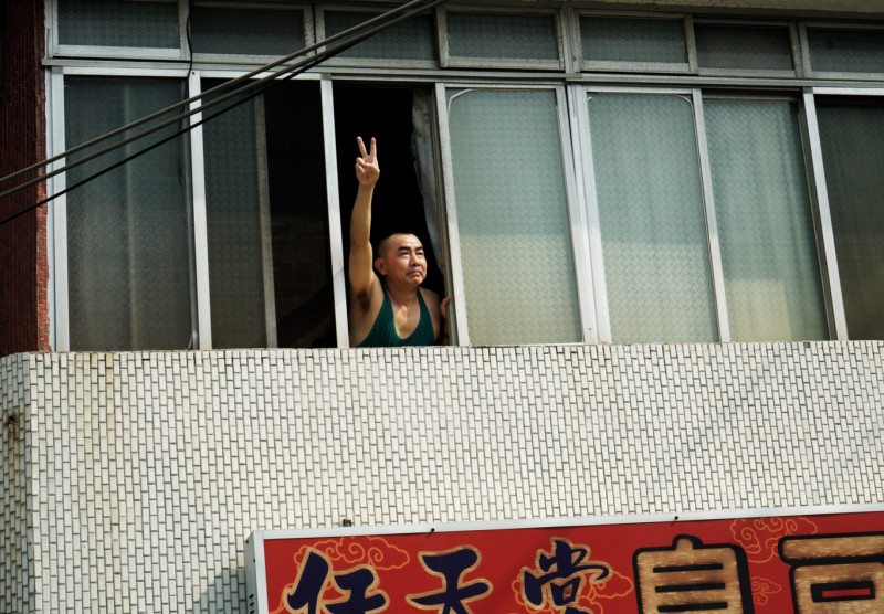 一位民眾在自家二樓窗口高舉著陳其邁競選號次的手勢。   圖：張良一/攝