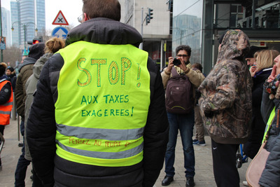 布魯塞爾12月15日第3波黃背心示威活動，抗議者在黃背心上寫下降稅訴求。   圖/中央社
