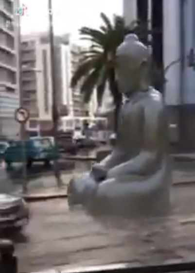 從影片中可以看出，一尊巨大佛像從高處街道緩緩順著水流漂向大馬路，旁邊還有車輛在行駛。   圖：翻攝自Youtube