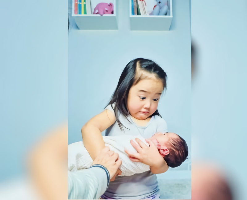網友分享女兒抱起新生妹妹的照片，女兒表情超母湯，笑翻大家。   圖／翻攝自 Reddit