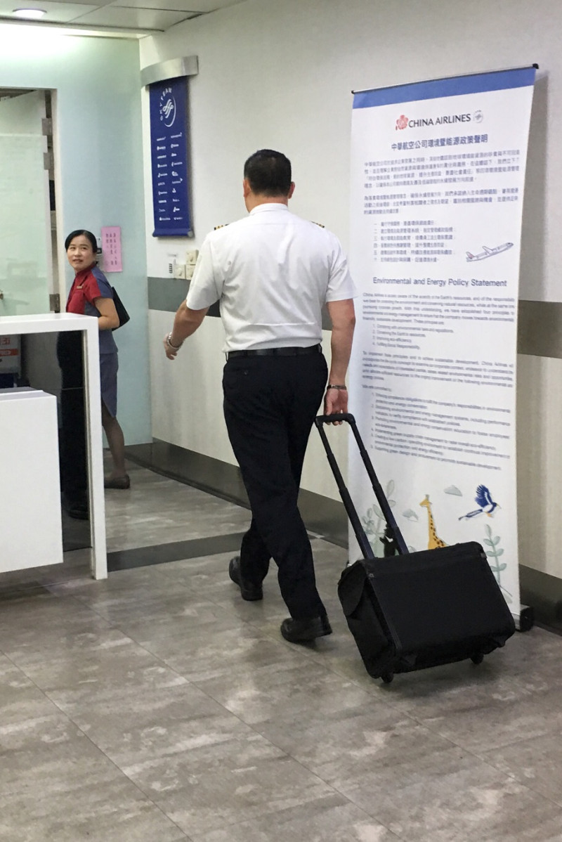 一位沒有參與罷工的華航機師拉著行李箱走進高雄小港國際機場出境大廳時，經過空蕩蕩的華航報到櫃檯，準備執勤。   圖：張良一攝