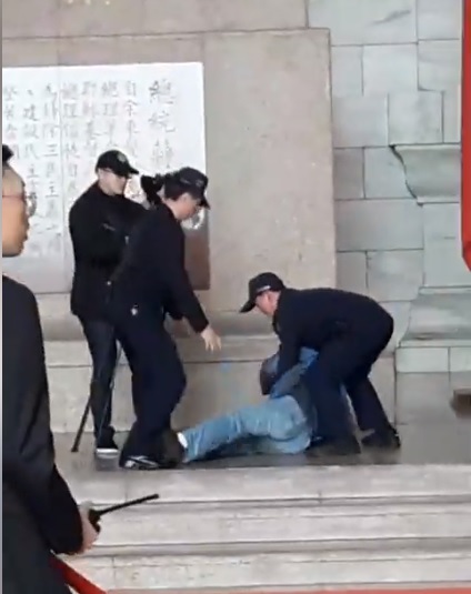 台灣國辦公室主任陳峻涵拿著魷魚糜朝蔣中正銅像丟擲，遭警方壓制在地。   圖：翻攝自台灣國辦公室臉書
