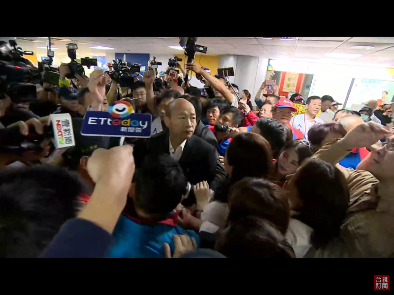 結束訪問，韓國瑜隨後經由二航廈南側公務門入境，並在航警引導下，向支持者揮手致意。由於現場群眾過於熱情，韓國瑜和李佳芬顯得寸步難行。   圖：翻攝自台視新聞直播