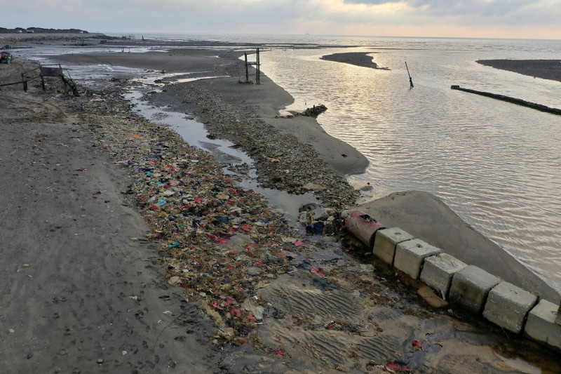 目前新街溪口仍可見廢棄布料及垃圾散布沙灘。   圖：桃園市政府環保局／提供