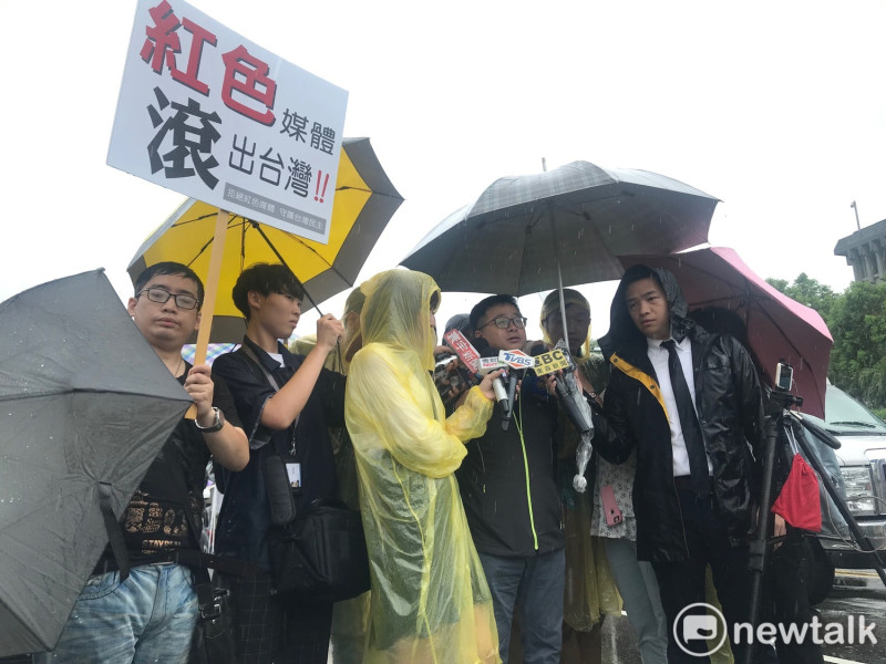 羅文嘉受訪時，有民眾高舉「紅色媒體、滾出台灣」標語。   圖：周煊惠 ／攝