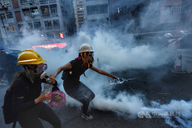 香港28日中環遮打花園追究警方用槍集會，演變為大規模「自主」遊行，香港警方晚間7時高舉黑旗，隨後施放催淚彈清場，示威者也以瓶裝水澆熄催淚彈。   圖：中央社提供。