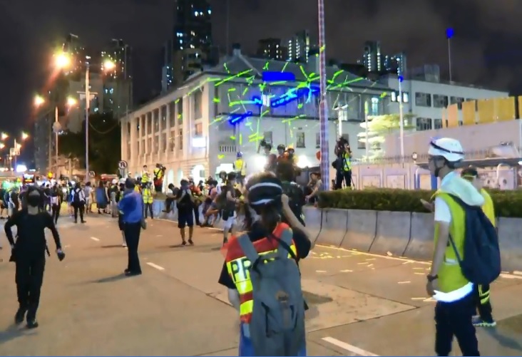 現場有人以雷射筆射向警署外牆，警方要求「雷射攻擊」警署的人馬上停止，否則將進行武力驅散。   圖：翻攝香港電台臉書影片
