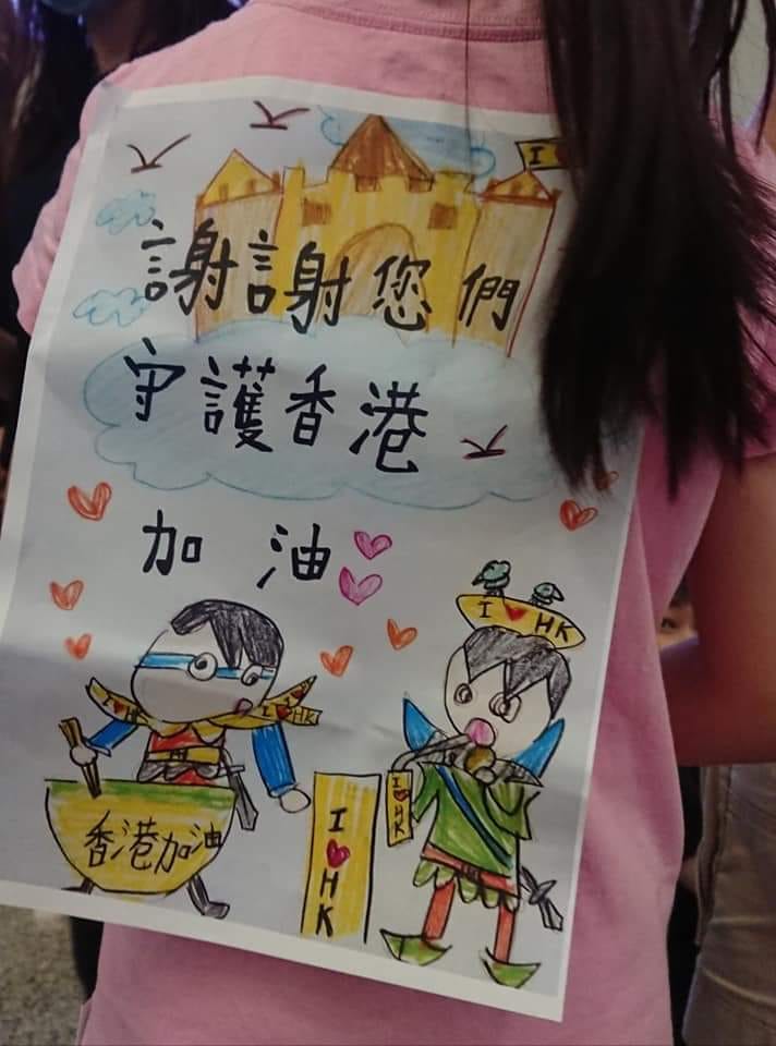 有網友在王丹臉書底下留言，指出當天在機場，還有一名小女孩與兩個小男生，發餅乾給現場留守的市民，背上同樣背著標語，寫著「謝謝您們守護香港」   圖：翻攝自王丹网站  Wang Dan's Page