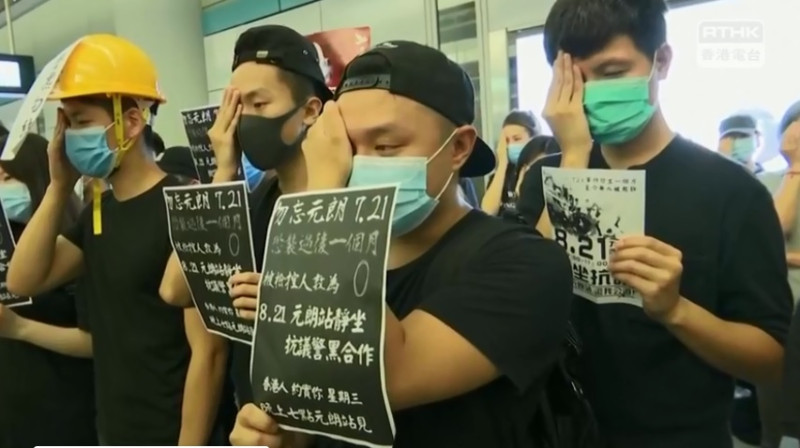 示威者穿黑衣戴口罩，手持「反對警黑合作」標語默站。   圖：翻攝香港電台視像新聞臉書