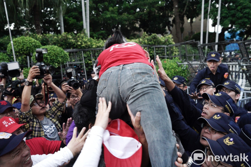 紅衣男子被抗議民眾抬起，試圖跨越拒馬，進入行政院，維安警察伸手阻攔。   圖：張良一／攝