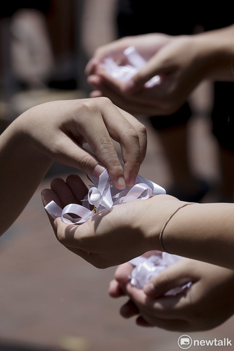 一位參加616反送中的民眾拿起一朵白色胸花，悼念前一晚在金鐘太古廣場跳樓的梁姓民眾，兩百萬加一人的香港民眾當天走上香港街頭，反對港府提出的送中條例。   圖：張良一 /攝
