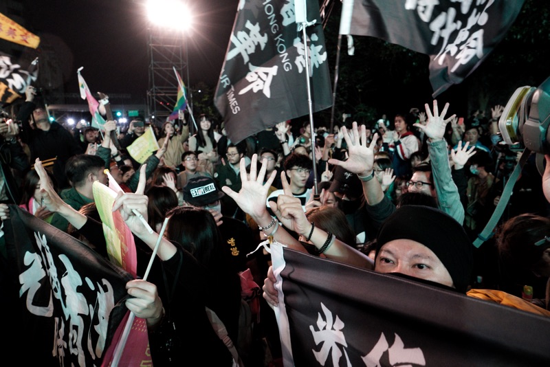 即時在台灣，港人還是在「光復香港時代革命」旗幟後，以不曝光方式比出五大訴求手勢。   圖：張良一/攝
