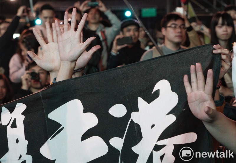 港人在「光復香港時代革命」旗幟後，以不曝光方式比出五大訴求手勢。   圖：張良一/攝