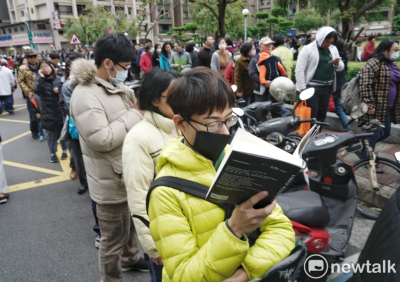 一位年輕人ㄧ邊排隊一邊看書，耐心等候。   圖：張良一/攝
