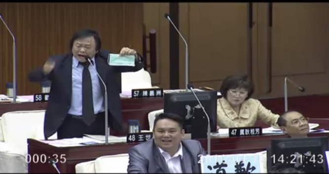王世堅於2016年4月12日在台北市議會開議時，曾對著正在發表施政報告的台北市長柯文哲痛批，要柯戴上口罩閉嘴。   圖：翻攝自台北市議會影音資訊網