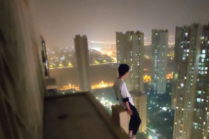 一名青年坐在建築邊緣，並把雙腳懸空在外。   圖：翻攝自新華社微信