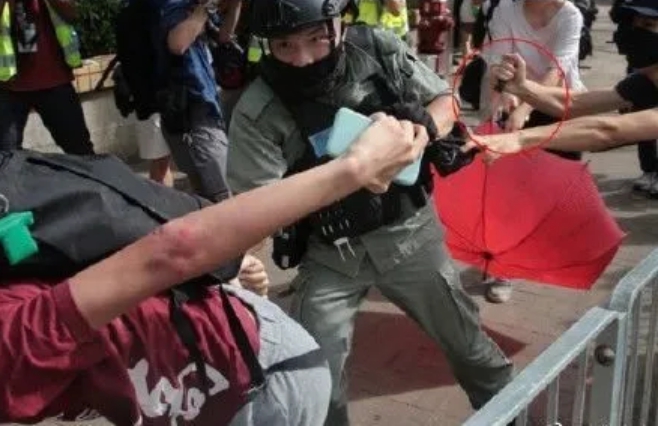 香港七一遊行刺警案中，持紅傘的白衣女子被警方懷疑是女哨兵。   圖：翻攝自北京日報