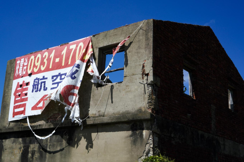 一棟靠近沙崙油庫的廢棄民宅，外牆上的航空城買賣廣告招牌被強風撕裂。   圖：張良一/攝