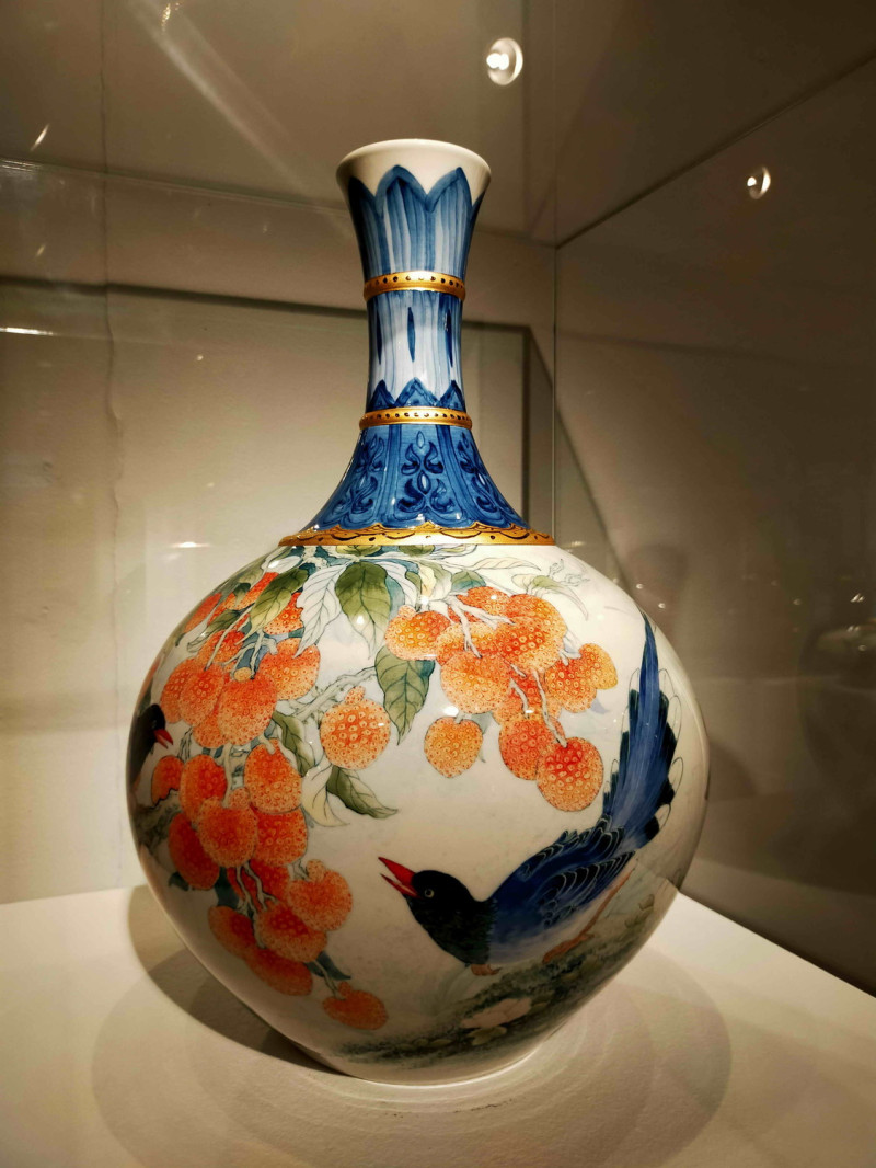 《荔枝藍鵲頸瓶》彩繪姿態優美的臺灣國鳥藍鵲，搭配火紅瑞澤的荔枝，組合出具時代特色的新樣式。    圖：鶯歌陶瓷博物館提供